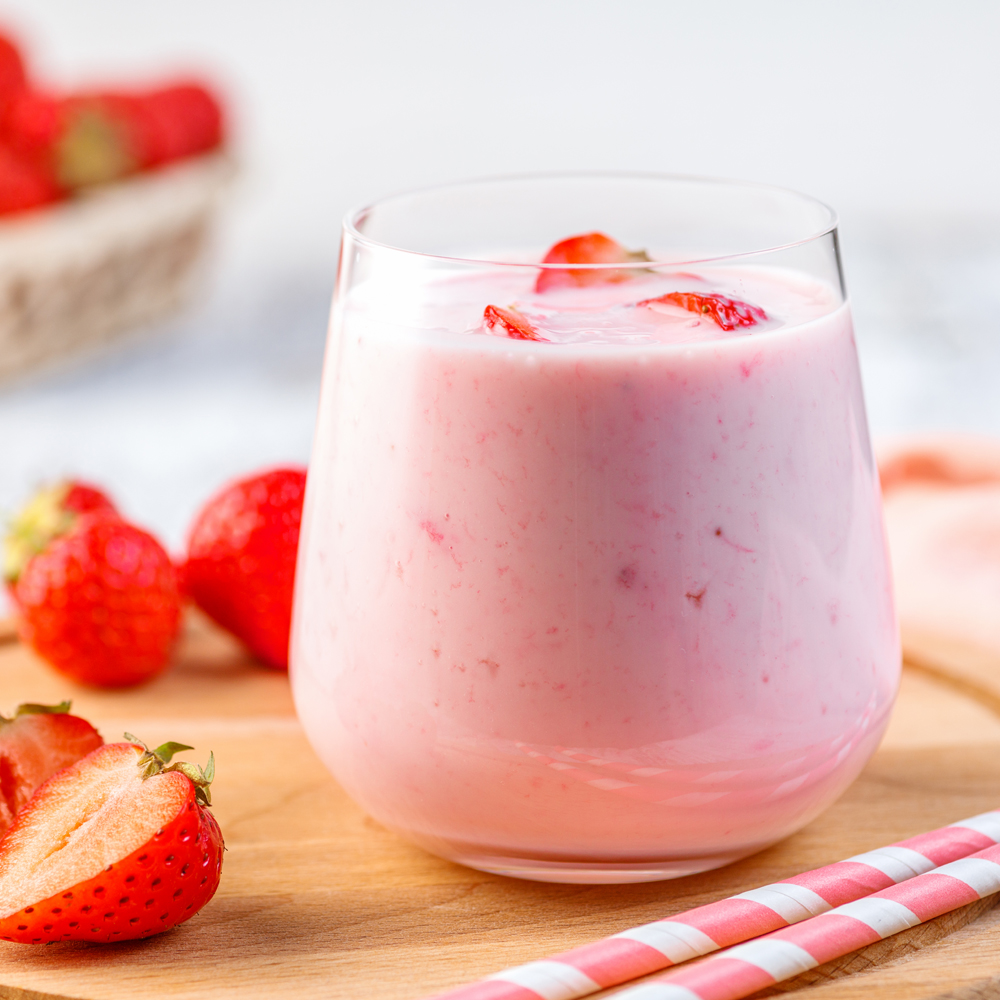 A glass of strawberry shake on a wooden board with fresh strawberries