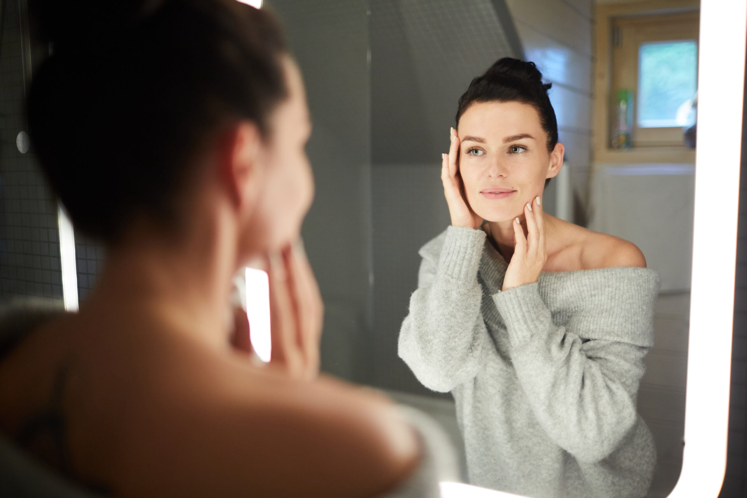 Woman looking in the mirror, touching her cheek