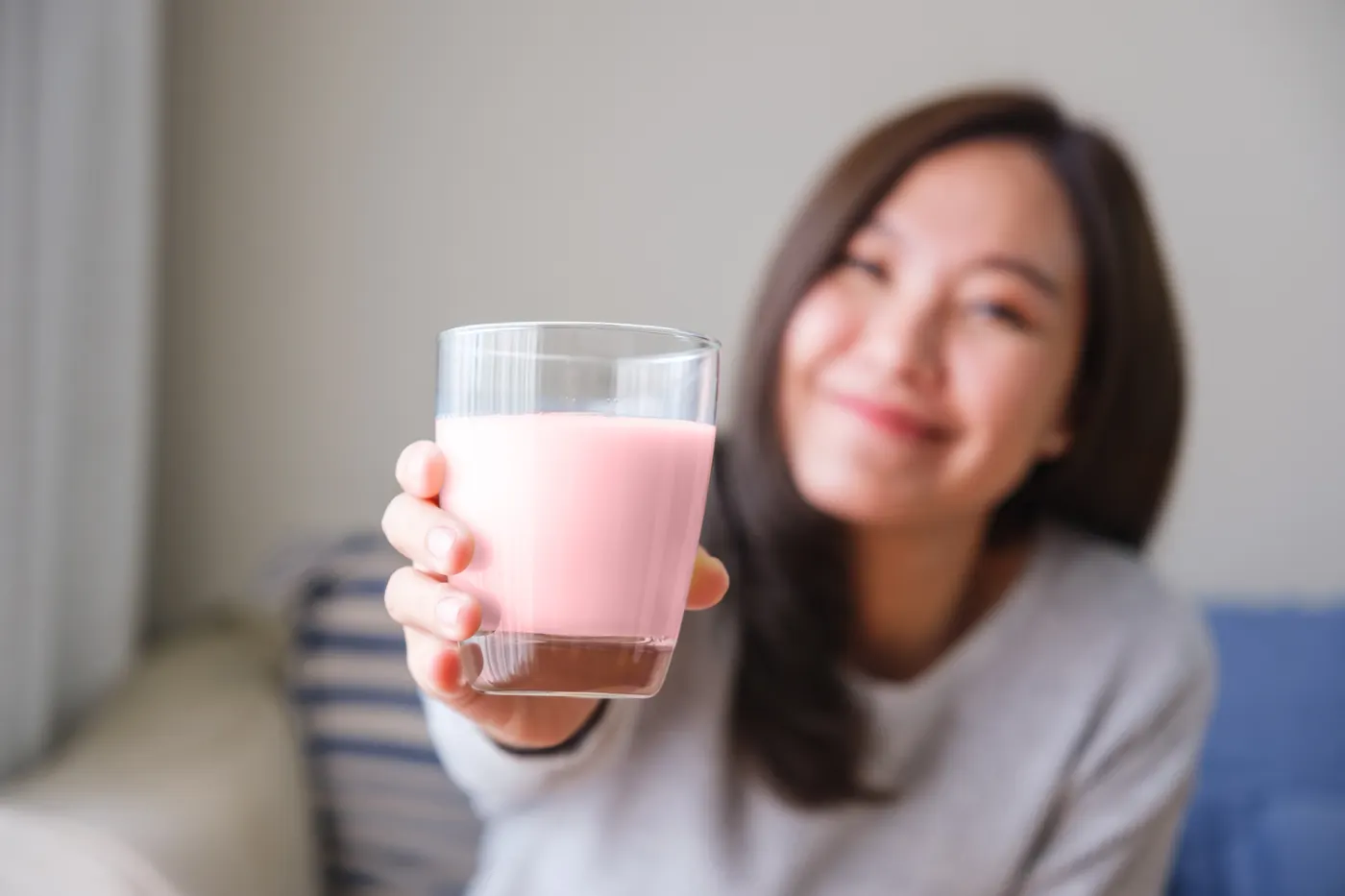 Smiling woman holding a glass of pink meal replacement shake