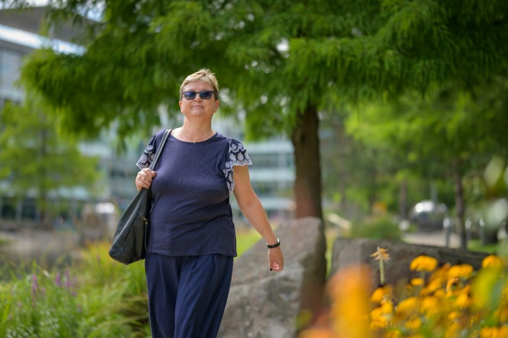 Woman walking through a sunny park on her way to work, carrying a shoulder bag